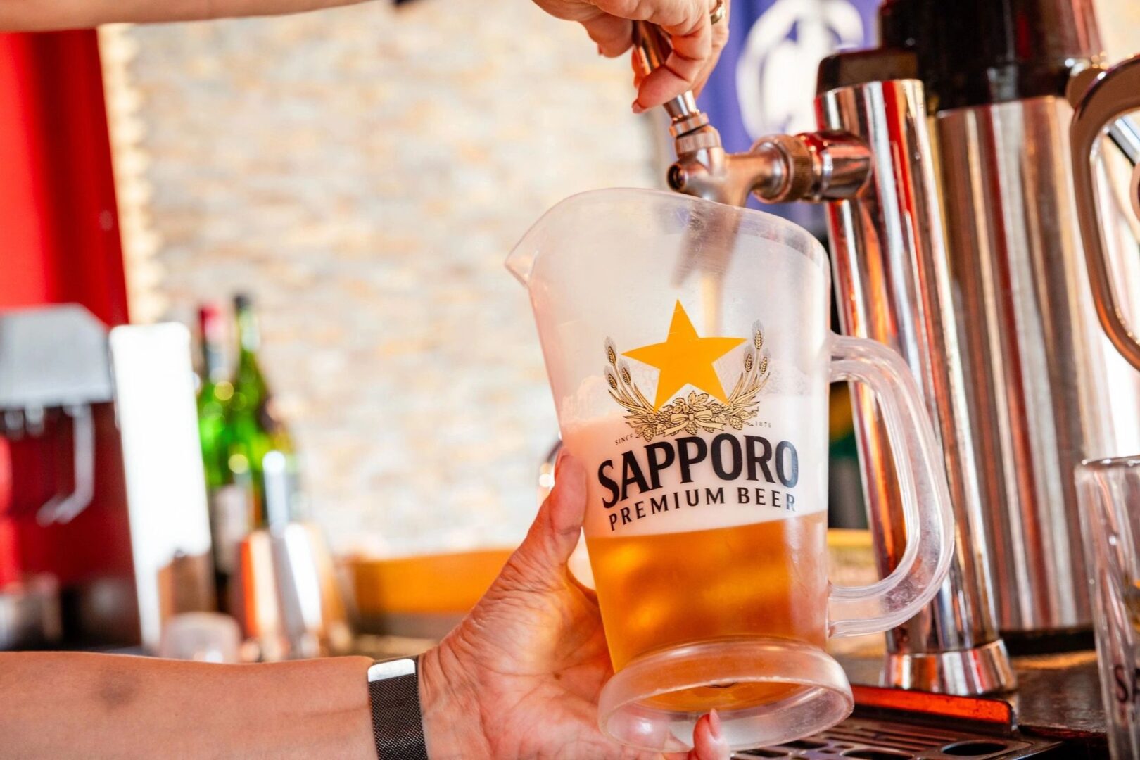 Person fills a pitcher with Sapporo beer from a tap at a bar.